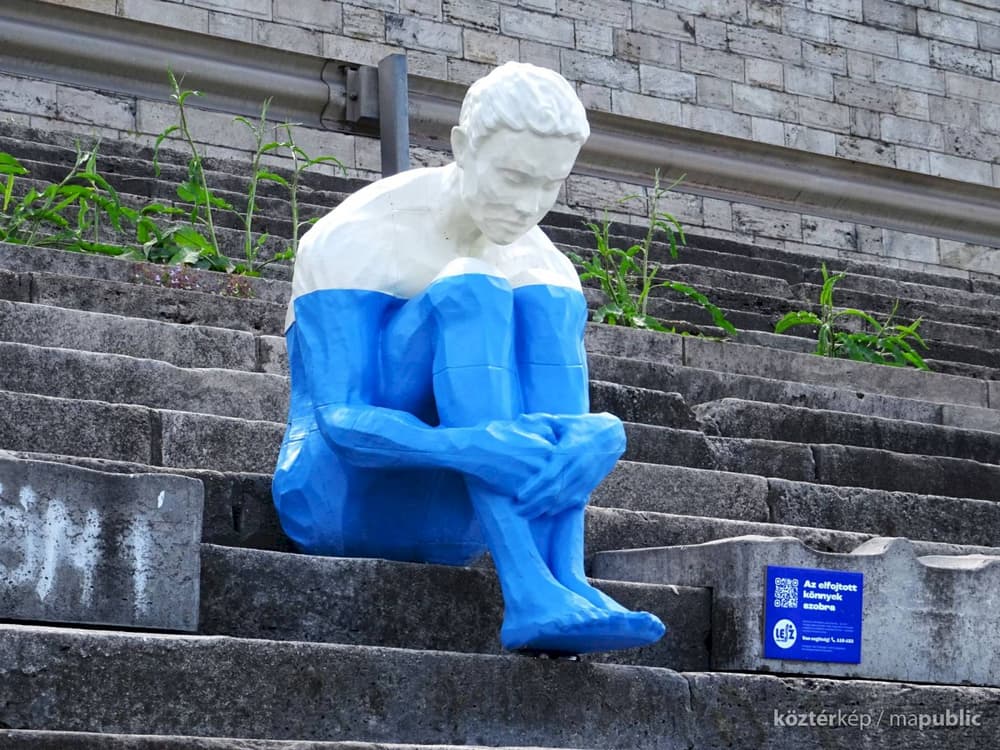 Close-up of the seated PETG sculpture on the embankment steps, with the LESZ Foundation plaque visible beside it