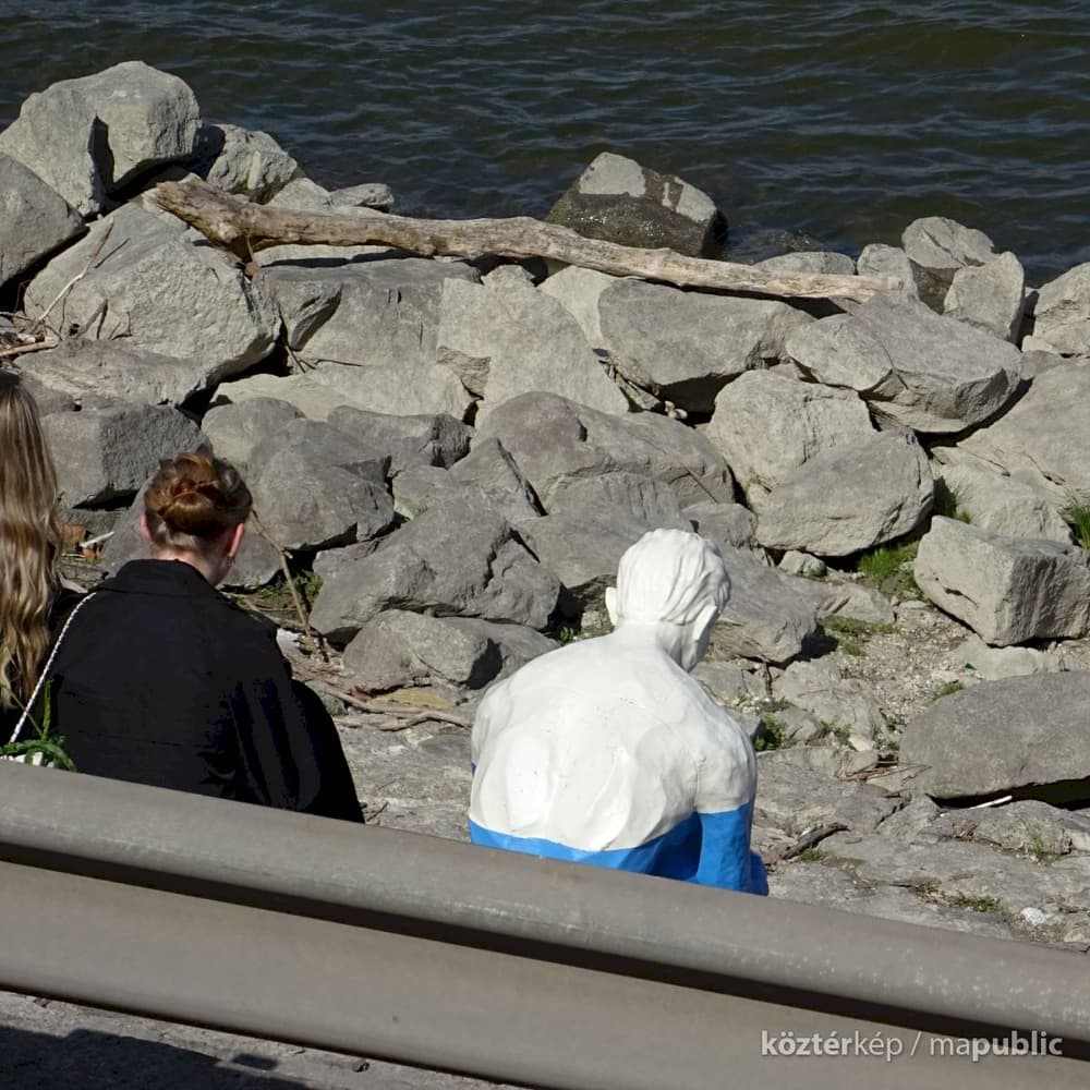 Rear view of the sculpture facing the Danube, surrounded by riprap stone at the water's edge